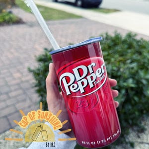 May include: A red insulated tumbler featuring the Dr Pepper logo in white. The tumbler has a silver lid and a clear straw. The text "Est. 1885" is visible. The tumbler holds 20 fl oz (1.25 pt) or 591 ml.