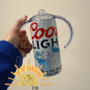 May include: A white and silver insulated tumbler with the Coors Light logo in red and black. The tumbler has a clear lid and handles. The design includes a mountain scene and the text "EST. 1978".