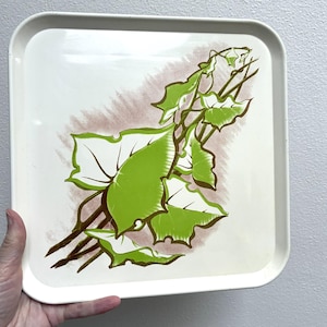 May include: A square, off-white serving tray with rounded corners. The tray features a green and brown leaf design on a white background. The leaves are a bright green color, and the stems are brown.