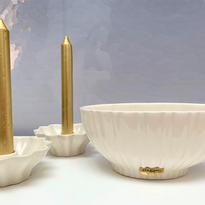 May include: Two off-white ceramic candle holders with scalloped edges, each containing a metallic gold taper candle, and one large off-white ceramic bowl with a scalloped exterior and a gold Haeger sticker on the front base.