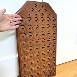 May include: A wooden pegboard with numerous evenly spaced pegs. The board is a warm brown color and has a rectangular shape with a slightly angled top. The pegs are cylindrical and protrude from the board's surface.