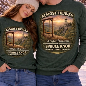 Könnte beinhalten: Zwei Personen tragen dunkelgrüne Langarmshirts mit dem Aufdruck "ALMOST HEAVEN" und "SPRUCE KNOB - WEST VIRGINIA" auf der Vorderseite. Die Shirts zeigen ein Landschaftsdesign mit einer Schaukel und einem Aussichtsturm. Sie tragen blaue Jeans und eine Mütze.