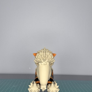 May include: A detailed figurine of a canine creature, viewed from the rear. The figure features a cream-colored mane and tail, with orange and black stripes on its body. The paws and ears are orange. The figurine is set against a gray background.