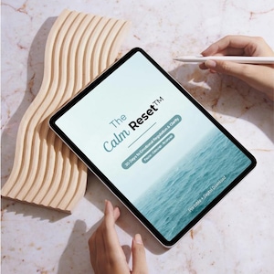 Könnte beinhalten: Ein digitales Tablet zeigt den Text "The Calm Reset" mit dem Untertitel "30 Tage zur emotionalen Regulierung & Klarheit". Der Bildschirm zeigt ein ruhiges Ozeanbild. Ein wellenförmiges Holzdekorstück befindet sich links.