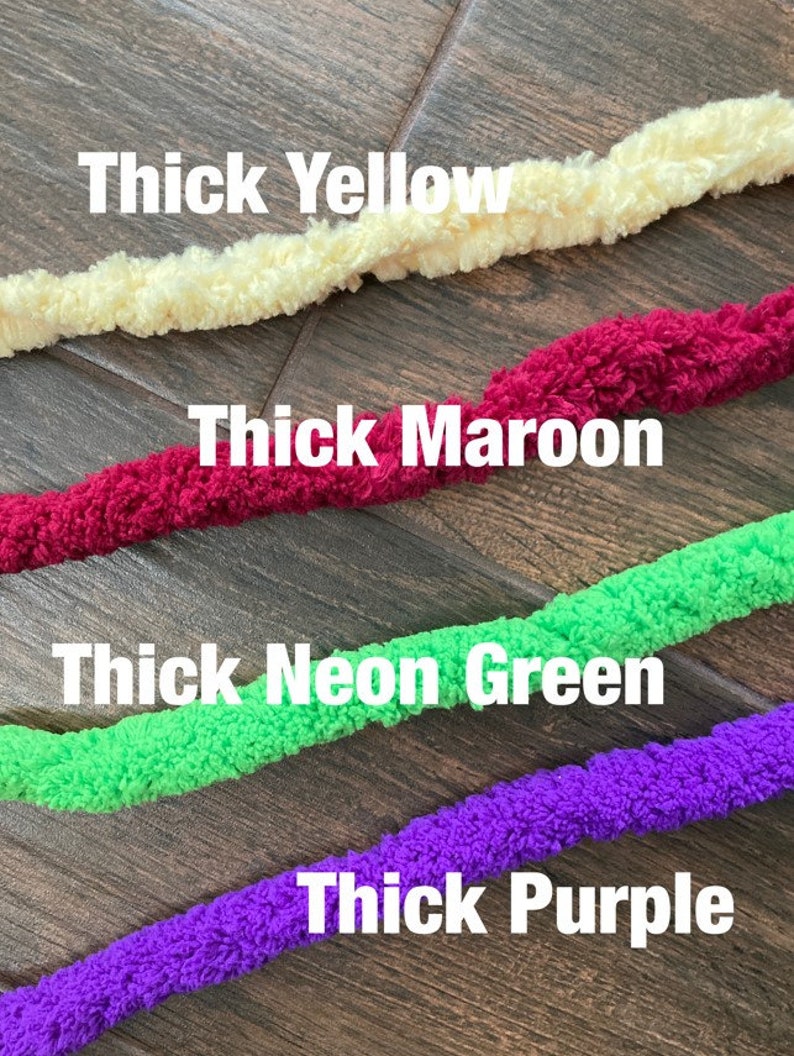 K&ouml;nnte beinhalten: Vier Str&auml;nge aus dickem, strukturiertem Garn in Gelb, Kastanienbraun, Neongr&uuml;n und Lila. Die Textbeschriftungen Thick Yellow, Thick Maroon, Thick Neon Green und Thick Purple befinden sich &uuml;ber jedem entsprechenden Garnstrang im Bild.