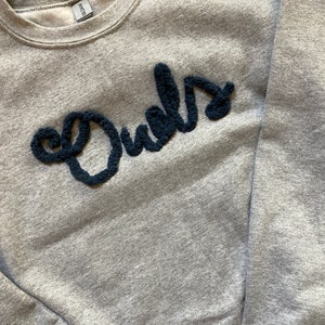 K&ouml;nnte beinhalten: Ein graumeliertes Sweatshirt mit Rundhalsausschnitt und dem Wort Owls in dunkelblauer, strukturierter, flauschiger und erhabener Garnschrift auf der Brust. Das Kleidungsst&uuml;ck hat lange &Auml;rmel, einen gerippten Kragen und ein Fleecefutter.