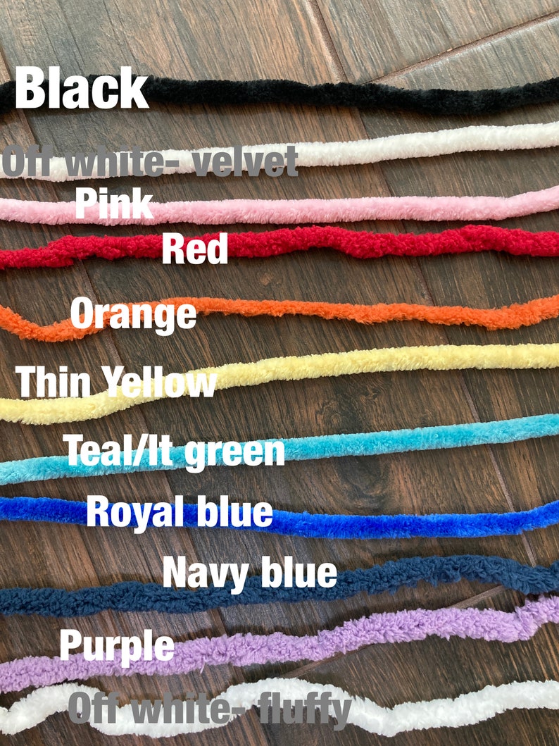 K&ouml;nnte beinhalten: Eine Sammlung von zehn flauschigen Garnstr&auml;ngen in verschiedenen Farben mit den Beschriftungen Black, Off white-velvet, Pink, Red, Orange, Thin Yellow, Teal/lt green, Royal blue, Navy blue, Purple und Off white-fluffy, horizontal gestapelt.