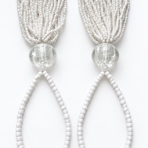 May include: A pair of decorative tassels featuring long strands of small, iridescent white beads. Each tassel is topped with a clear, spherical glass bead with internal crackle detailing, connected to a loop of opaque white beads.