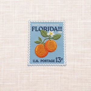 May include: Embroidered patch resembling a vintage Florida postage stamp. The design features two oranges, green leaves, and a white flower against a light blue background. Text includes "FLORIDA!!!" and "U.S. POSTAGE 13¢".
