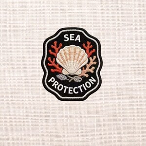 May include: Embroidered patch featuring a seashell, coral, and the words "SEA PROTECTION." The patch has a black border with white lettering and is set against a textured, off-white background. The seashell is beige and the coral is orange.