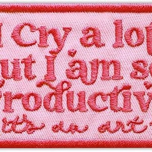 May include: Pink embroidered patch with the text "I Cry a lot but I am so Productive as an art" in red thread. The patch has a red border and is rectangular in shape.