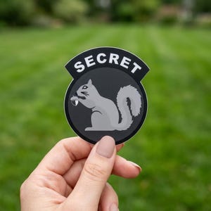 May include: A white ceramic mug with a black handle and the text "But First, Coffee" in a black, handwritten-style font. The mug is on a white surface.