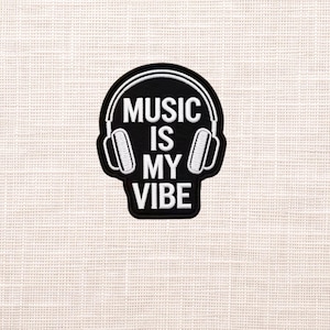 May include: Black patch with white embroidered text and design. The patch features the words "MUSIC IS MY VIBE" in a bold font, with a white outline. The design includes a pair of white headphones.