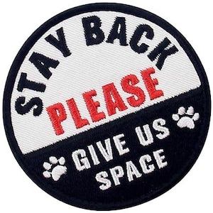 May include: Round patch with the words "STAY BACK PLEASE" in black and red, and "GIVE US SPACE" in white. Features two paw prints. The patch has a black border.