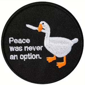 May include: Embroidered patch with a white goose and orange beak and feet on a black background. The text "Peace was never an option" is in white. The patch is round.