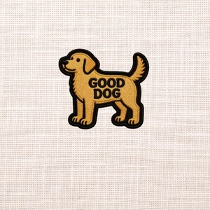 May include: A tan and black embroidered patch in the shape of a dog. The patch has the words "GOOD DOG" in black block letters. The dog is a golden color with a black outline.