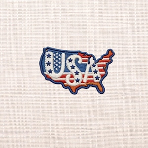 May include: An embroidered patch in the shape of the United States map. The design features the letters USA in white with blue stars, set against a background of horizontal red and white stripes, all outlined with a thick dark blue border.