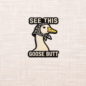 May include: A patch featuring a goose wearing a headscarf. The text "SEE THIS" is above the goose, and "GOOSE BUTT" is below. The goose has a yellow beak and is set against a white background.