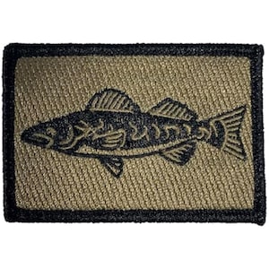 May include: A rectangular patch featuring a detailed black fish design on a tan background. The fish is outlined with intricate details, and the patch has a black border. The patch is likely for clothing or accessories.
