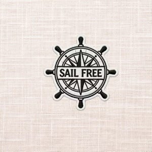 May include: A black and white embroidered patch featuring a ship's wheel design with the text "SAIL FREE" in a rectangular banner. The patch has a nautical theme and is set against a textured, off-white background.