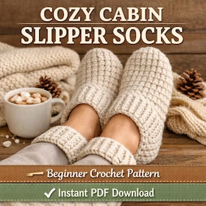 May include: A pair of cream-coloured, chunky knit slipper socks. The text "Cozy Cabin Slipper Socks" is displayed at the top. A mug of hot chocolate, a knitted blanket, and pine cones are also visible. The text "Beginner Crochet Pattern" and "Instant PDF Download" are also visible.