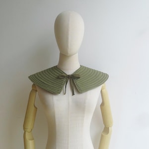 May include: A green quilted fabric collar with a matching green satin ribbon tied in a bow at the centre.