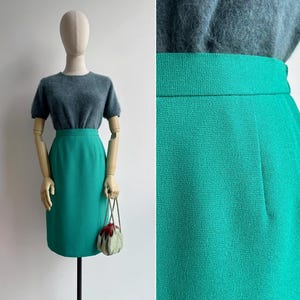 Op de afbeelding: Een rok met hoge taille en knielengte in een levendige smaragdgroene kleur met een textuur van geweven stof. De rok heeft een strak, recht silhouet met een gestructureerde tailleband en een subtiel verticaal naaddetail aan de voorzijde.