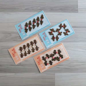 Puede incluir: Cuatro paquetes de botones decorativos con un diseño floral. Cada paquete tiene un esquema de color diferente: rojo, azul, blanco y rosa. Los paquetes están etiquetados en caracteres chinos.