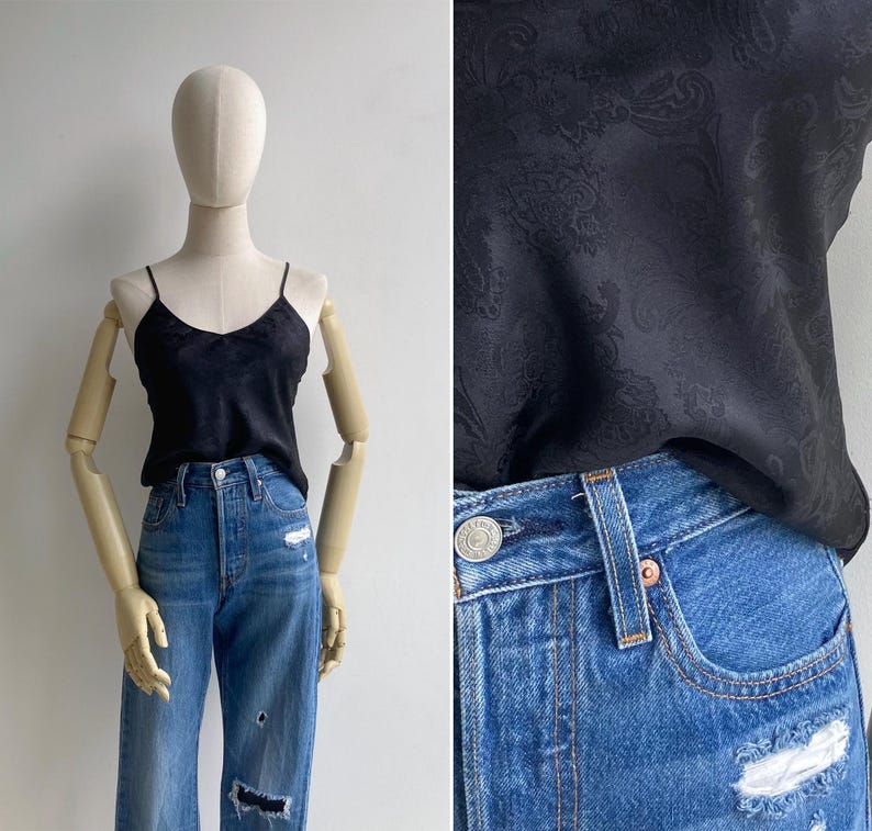 A mannequin wears a 90s silky cami tank with a woven paisley texture tucked not a pair of high waisted blue jeans