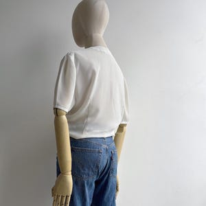 Back view of a mannequin in a 1980s vintage white draped blouse with short sleeves.