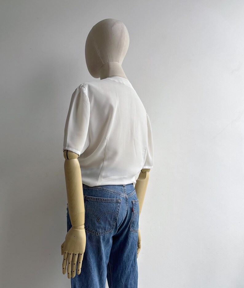 Back view of a mannequin in a 1980s vintage white draped blouse with short sleeves.