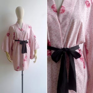 A mannequin wears s 50s pink silk haori kimono robe tied at the waist with a black sash. It has an open wrap front, shibori tie dye print and painterly pink floral motifs all over.