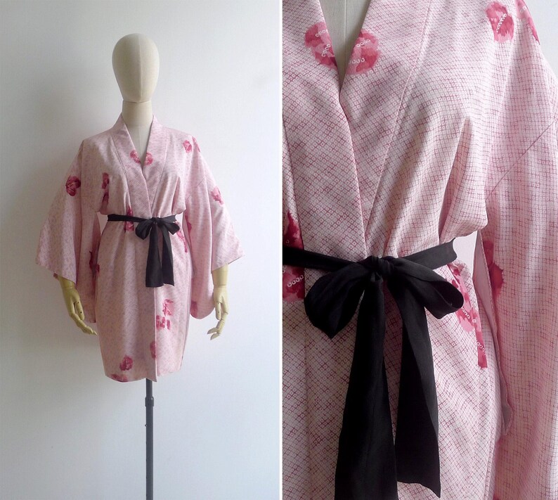 A mannequin wears s 50s pink silk haori kimono robe tied at the waist with a black sash. It has an open wrap front, shibori tie dye print and painterly pink floral motifs all over.
