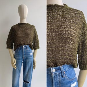 Puede incluir: Top de punto verde oliva con mangas cortas y cuello redondo. El top presenta un diseño texturizado de tejido abierto. Se combina con vaqueros azules con detalles desgastados.