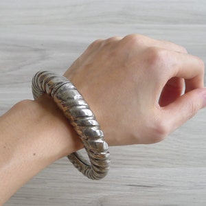 May include: A silver bangle bracelet with a twisted design. The bracelet is thick and has a smooth, polished finish.