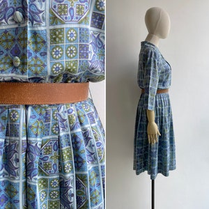 May include: A vintage dress with a blue, green, and purple geometric pattern. The dress features a button-down top, a pleated skirt, and a brown belt. The dress is displayed on a mannequin.