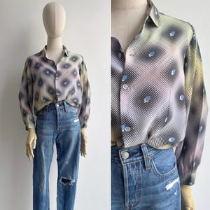 May include: A long-sleeve button-down shirt featuring a gradient moiré pattern in shades of black, white, and soft yellow, accented with small blue geometric shapes. The shirt is paired with blue denim jeans that have distressed knee detailing.