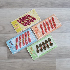 May include: Four packages of decorative embellishments for clothing. Each package contains six pieces of red, pink, or black fabric with gold or red beads. The packages are labeled with Chinese characters.