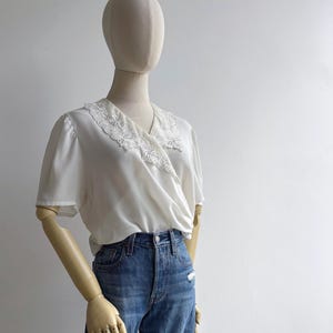 Angled view of a mannequin in a retro 80s sweet lace collar white blousy top with short sleeves & a v-neck wrap design.