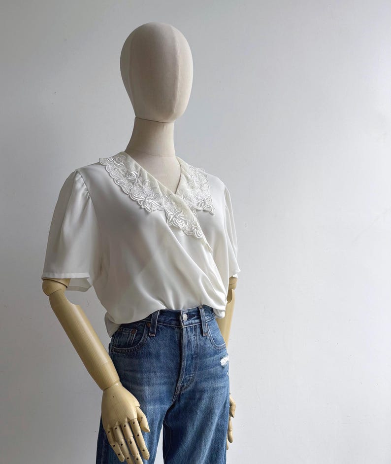 Angled view of a mannequin in a retro 80s sweet lace collar white blousy top with short sleeves & a v-neck wrap design.