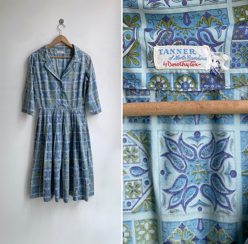 May include: Vintage blue and green patterned dress with a collared neckline and three-quarter sleeves. The dress features a button-down front and a pleated skirt. The tag reads "TANNER of North Carolina by Dorothy Cox".