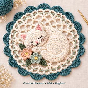 May include: A round crochet doily featuring a sleeping white cat in the center, accented with a pink and green flower. The doily has a cream-colored lattice pattern and a scalloped teal border. Text at the bottom reads Crochet Pattern PDF English.