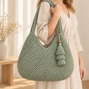 May include: A sage green crochet shoulder bag featuring a textured stitch pattern with diagonal raised lines. The bag includes a matching three-tiered tassel ornament attached to a single wooden bead on the side strap, providing a cohesive look.