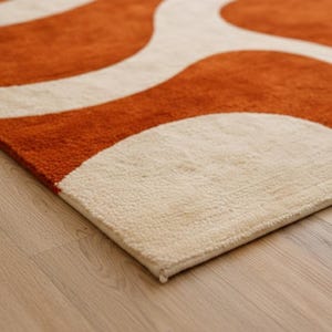 A corner angle of the Large Burnt Orange Rug for Living Room laying flat on a light wood floor. This shot displays the durable backing and the vibrant Retro 70s design, perfect for Mid Century Modern Decor styling.