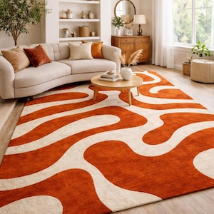 A high-quality Hand Tufted Wool Rug featuring a Retro 70s Wavy Abstract pattern in vibrant Burnt Orange and cream colors. This Large Burnt Orange Rug for Living Room is styled under a curved sofa in a bright, modern room with Mid Century Modern Decor.