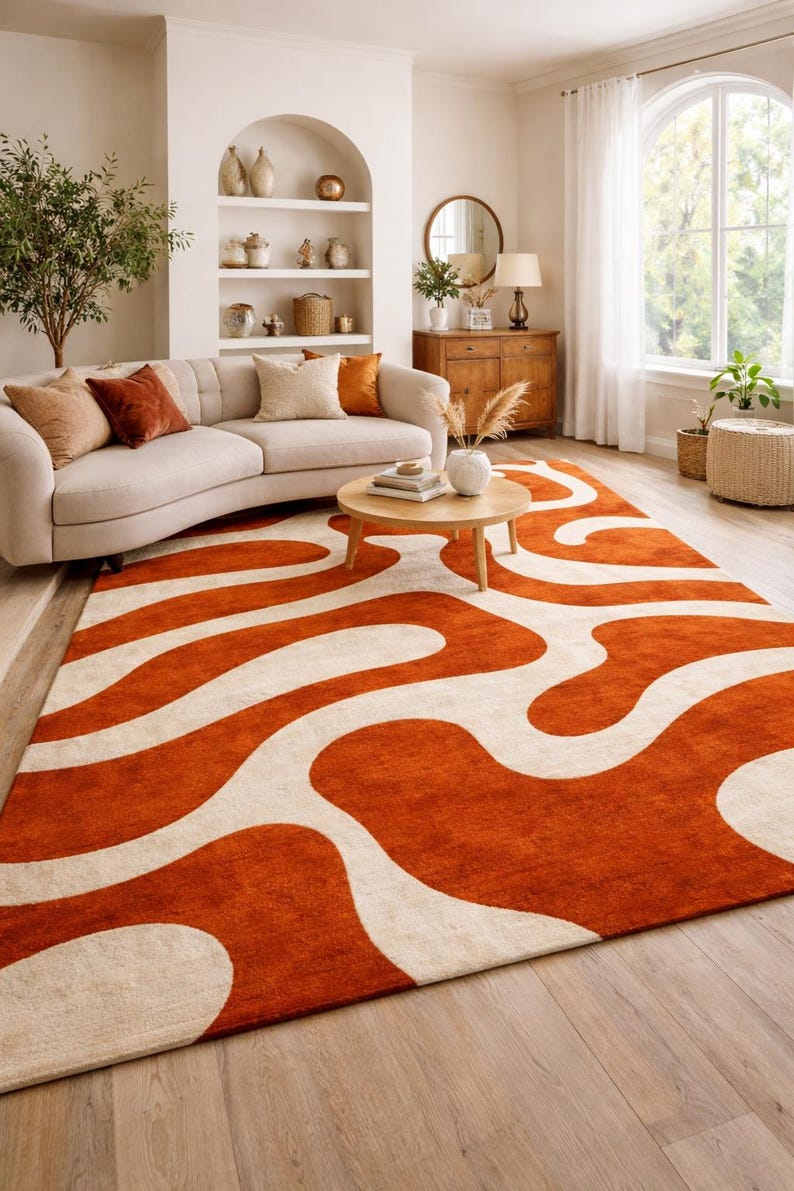 A high-quality Hand Tufted Wool Rug featuring a Retro 70s Wavy Abstract pattern in vibrant Burnt Orange and cream colors. This Large Burnt Orange Rug for Living Room is styled under a curved sofa in a bright, modern room with Mid Century Modern Decor.