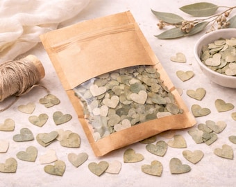 May include: A kraft paper bag with a clear window filled with heart-shaped eucalyptus leaves. Scattered around are more heart-shaped leaves in shades of green and cream. A small bowl of leaves and a spool of twine are also present.