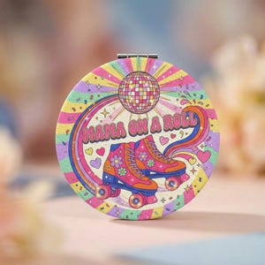 Peut inclure: Un miroir de poche rond avec un design rétro coloré. Il présente une boule disco, des patins à roulettes et le texte "MAMA ON A ROLL". Le fond est orné d'un arc-en-ciel et d'un motif d'éclat d'étoile, avec des cœurs et des fleurs.