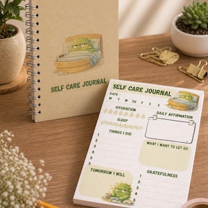 May include: A spiral-bound self-care journal and a notepad. The journal and notepad feature a cartoon cactus character in bed. The notepad includes sections for daily affirmations, hydration, sleep, and gratitude. The journal and notepad are on a wooden surface.