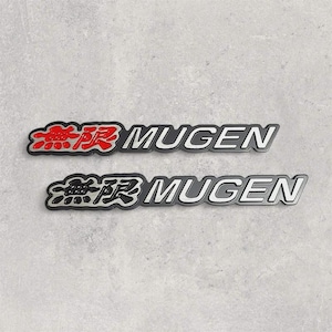 Puede incluir: Dos pegatinas con el emblema de Mugen. La pegatina superior tiene caracteres japoneses rojos y la palabra "MUGEN" en blanco. La pegatina inferior tiene el mismo diseño, pero los caracteres japoneses son negros y la palabra "MUGEN" es blanca.